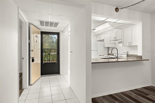 kitchen with kitchen peninsula, white cabinetry, dark stone counters, light wood-type flooring, and white fridge