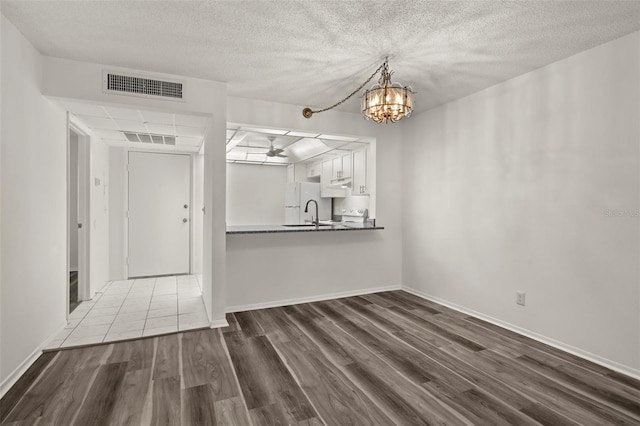 unfurnished dining area featuring sink, a textured ceiling, wood-type flooring, and ceiling fan with notable chandelier