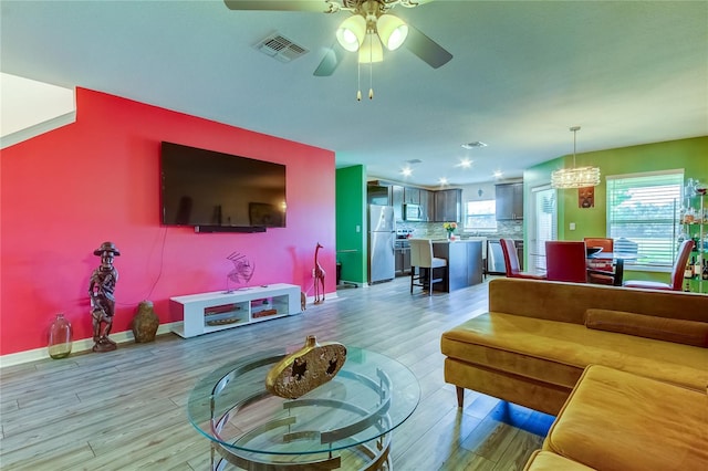 living room with ceiling fan with notable chandelier and light wood-type flooring