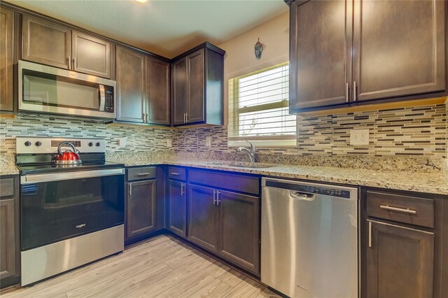 kitchen with sink, dark brown cabinets, light hardwood / wood-style flooring, appliances with stainless steel finishes, and light stone countertops