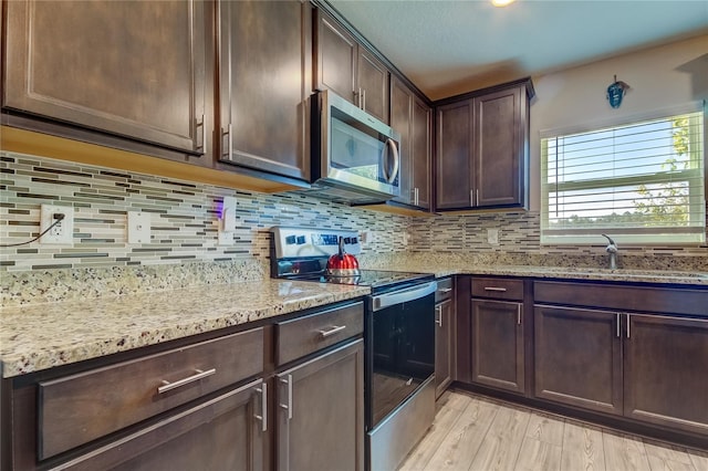 kitchen featuring light stone countertops, stainless steel appliances, light wood-type flooring, dark brown cabinets, and sink