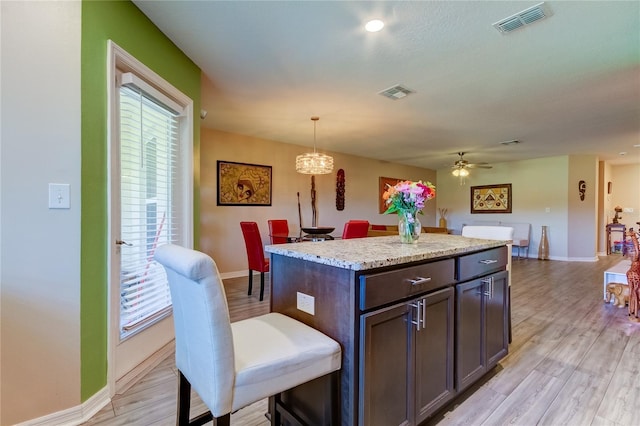 kitchen featuring dark brown cabinets, ceiling fan with notable chandelier, a kitchen island, light hardwood / wood-style flooring, and decorative light fixtures