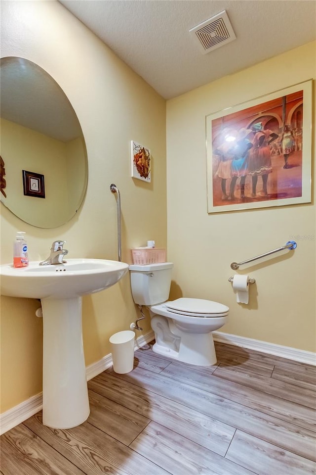 bathroom with wood-type flooring, a textured ceiling, and toilet