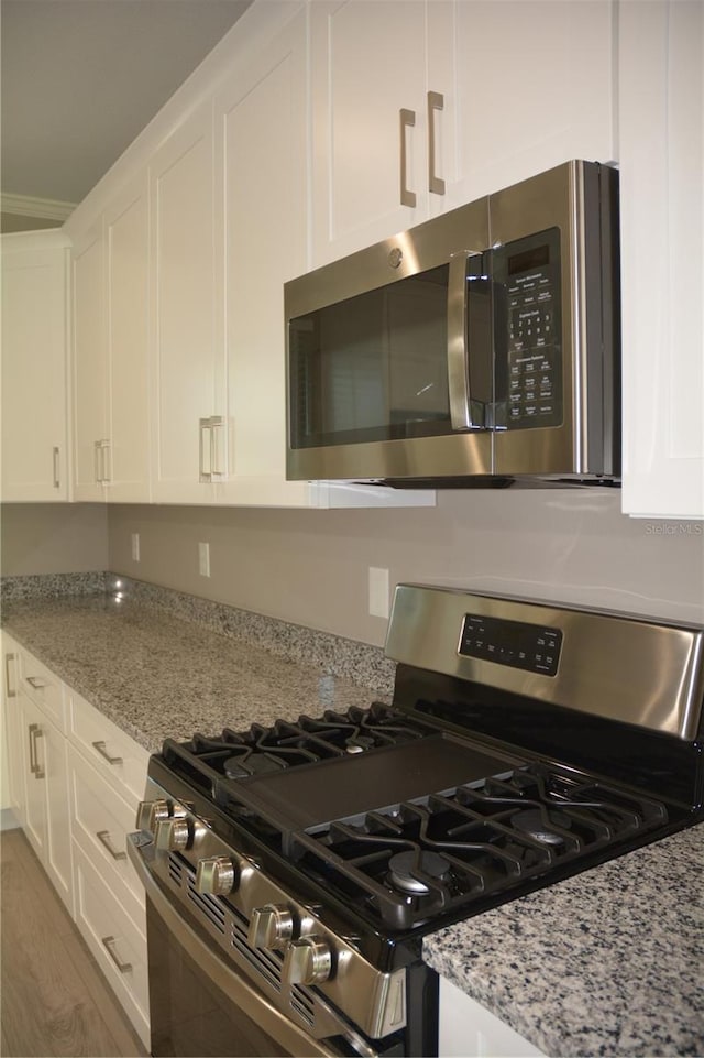 kitchen with light stone counters, white cabinets, hardwood / wood-style flooring, and appliances with stainless steel finishes