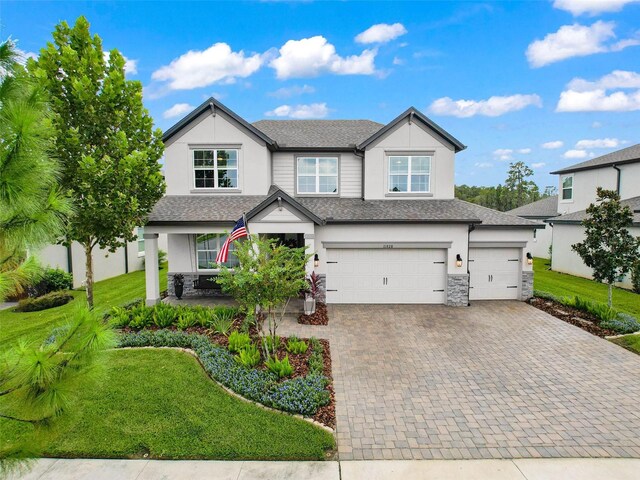 view of front of home with stucco siding, a front lawn, a garage, stone siding, and decorative driveway