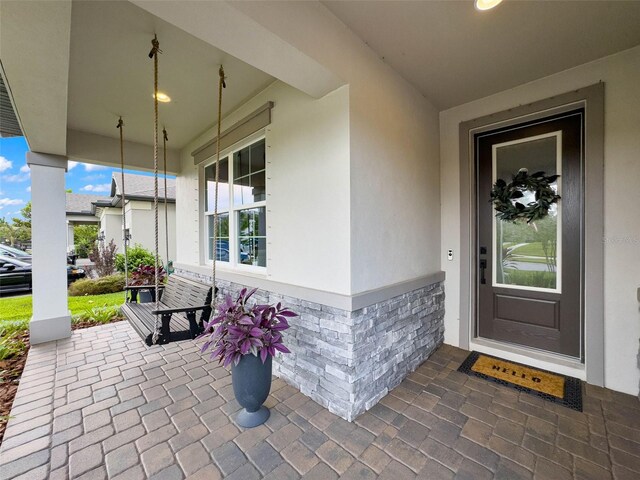 doorway to property with covered porch, brick siding, and stucco siding