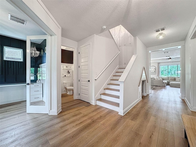foyer entrance featuring light wood-type flooring, a textured ceiling, stairway, and visible vents