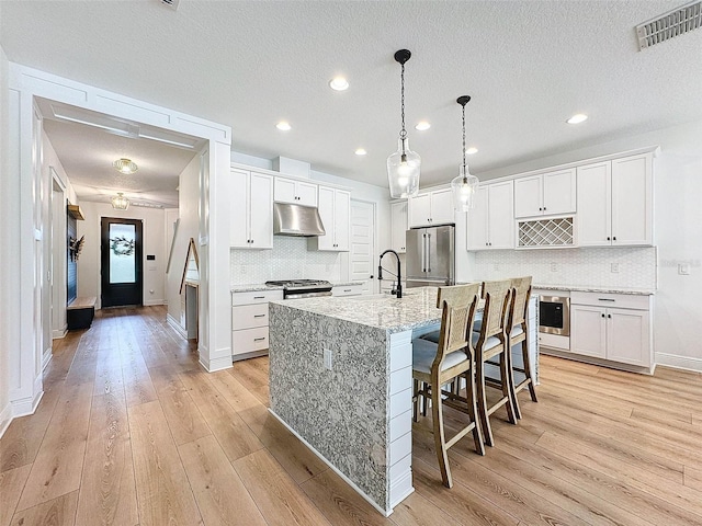 kitchen with light wood-type flooring, appliances with stainless steel finishes, under cabinet range hood, and visible vents