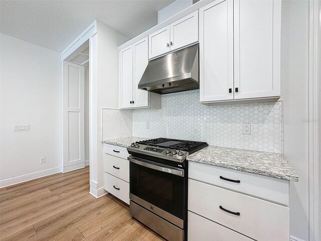 kitchen with light wood-type flooring, under cabinet range hood, decorative backsplash, light stone countertops, and stainless steel range with gas stovetop