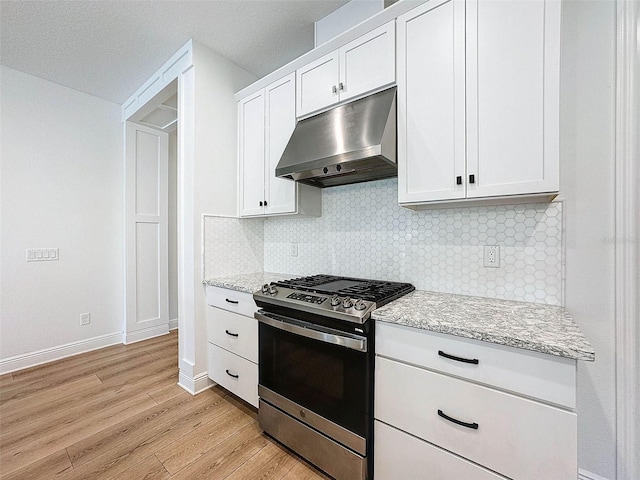 kitchen featuring gas stove, under cabinet range hood, light wood-style floors, light stone counters, and backsplash