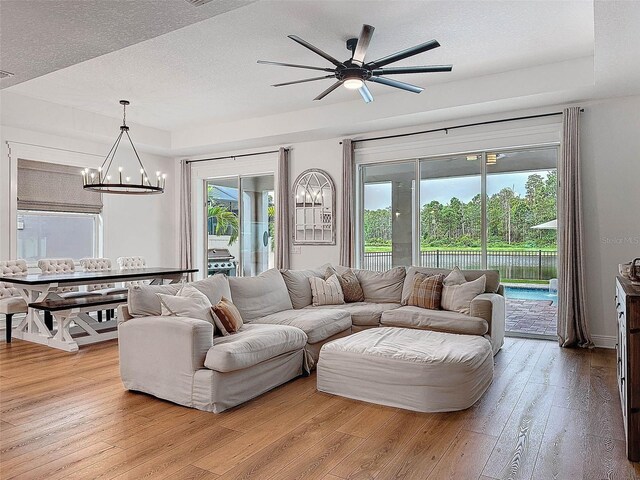 living room featuring a chandelier, plenty of natural light, a raised ceiling, and light wood-style flooring