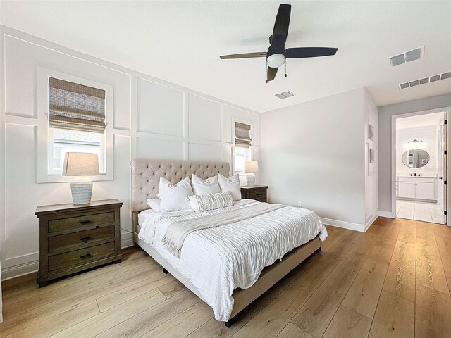 bedroom featuring a ceiling fan, a decorative wall, light wood-style floors, and visible vents