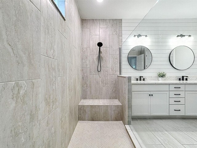 full bath featuring double vanity, tiled shower, and a sink