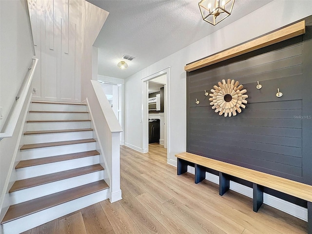 stairway featuring an inviting chandelier, baseboards, a textured ceiling, visible vents, and wood finished floors