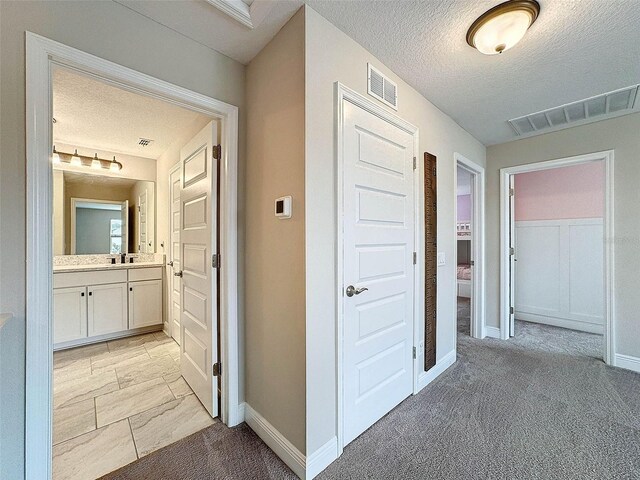 hallway featuring visible vents, light colored carpet, a textured ceiling, and a sink