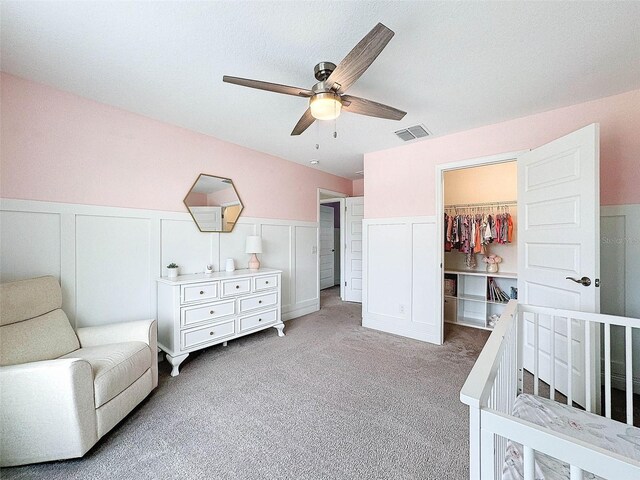 bedroom featuring visible vents, a wainscoted wall, a walk in closet, a closet, and light colored carpet