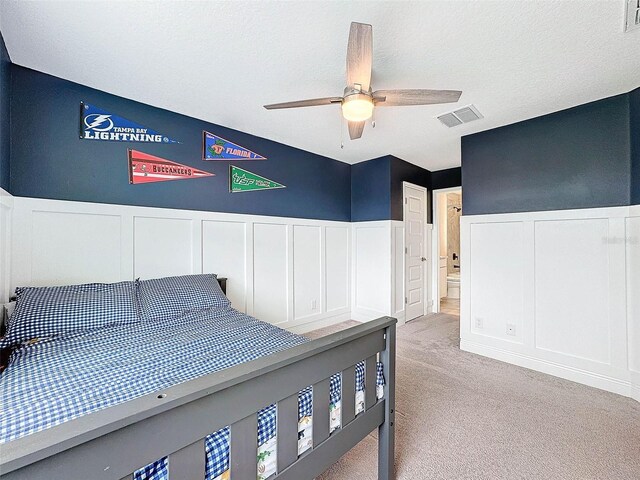 bedroom with visible vents, light carpet, a textured ceiling, and a wainscoted wall