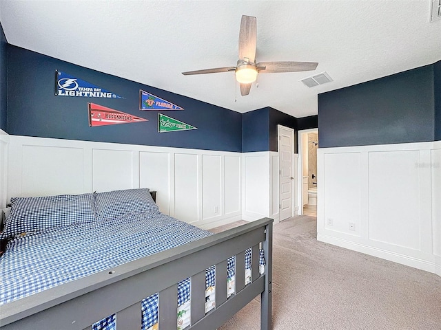 bedroom with a wainscoted wall, light carpet, a textured ceiling, and visible vents