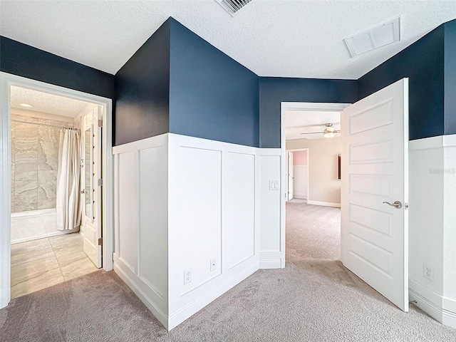 corridor with a wainscoted wall, a textured ceiling, visible vents, and carpet