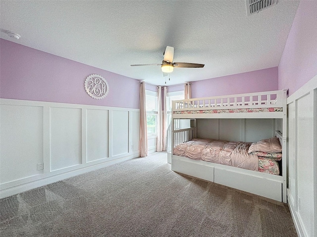 unfurnished bedroom with carpet flooring, a textured ceiling, a wainscoted wall, visible vents, and a decorative wall