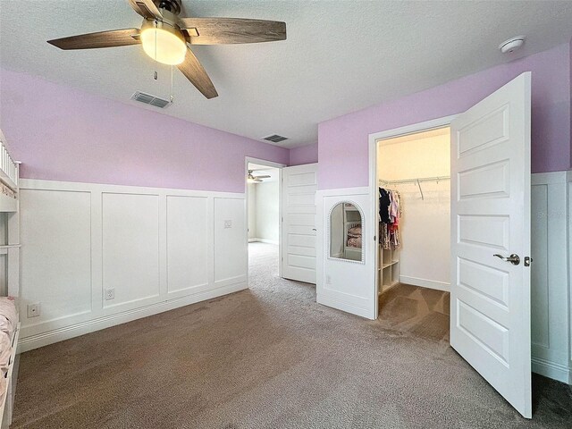 unfurnished bedroom featuring visible vents, carpet, a walk in closet, and a decorative wall