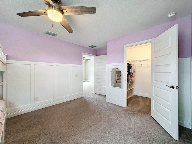 unfurnished bedroom with carpet flooring, a decorative wall, a spacious closet, and visible vents