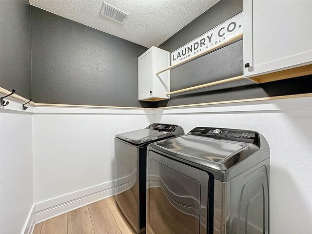 clothes washing area with visible vents, washing machine and clothes dryer, light wood-style flooring, cabinet space, and a textured ceiling