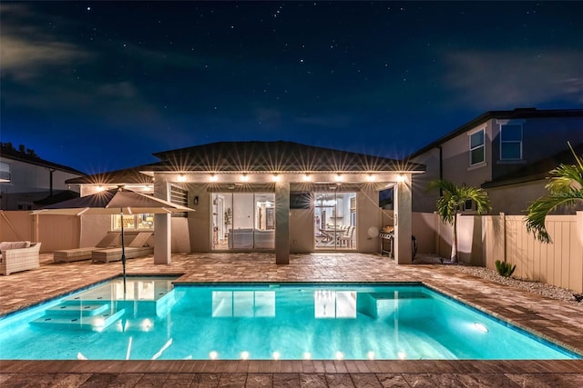 pool at night featuring fence, an outbuilding, a patio area, and a fenced in pool