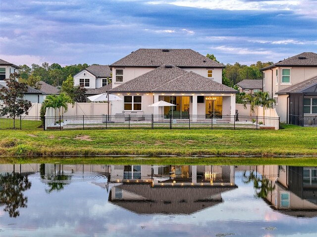 rear view of house with a yard, a water view, fence, and stucco siding