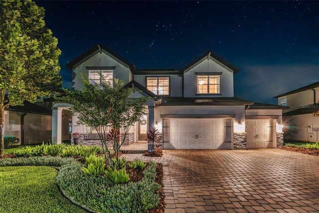 view of front facade with decorative driveway, stone siding, a garage, and stucco siding