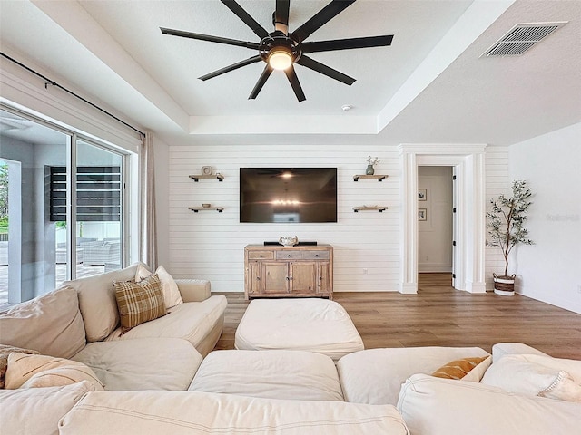 living area with a raised ceiling, wood finished floors, visible vents, and baseboards