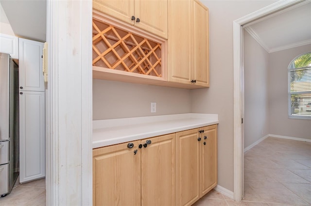 kitchen with stainless steel fridge, light tile patterned flooring, crown molding, and light brown cabinetry