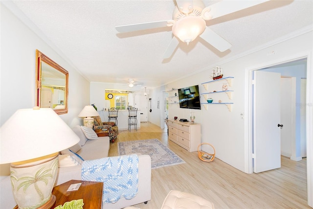 living room featuring ornamental molding, light hardwood / wood-style floors, ceiling fan, and a textured ceiling