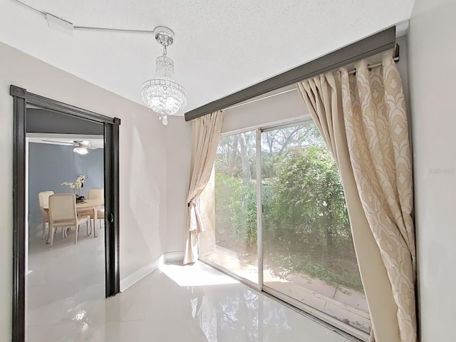 doorway to outside featuring ceiling fan with notable chandelier, rail lighting, and a textured ceiling