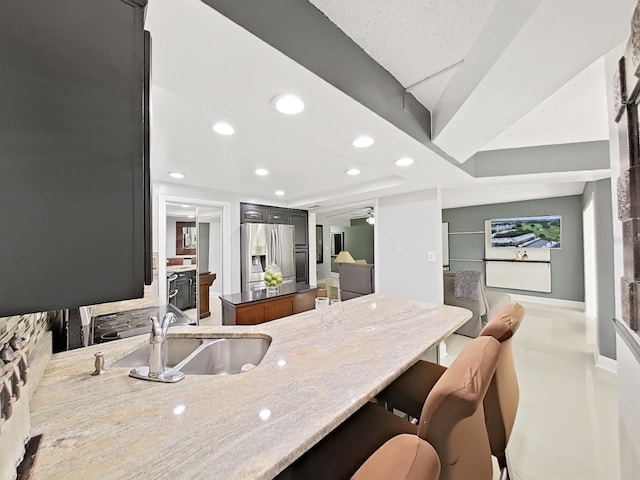 kitchen with kitchen peninsula, stainless steel fridge with ice dispenser, sink, and light stone counters