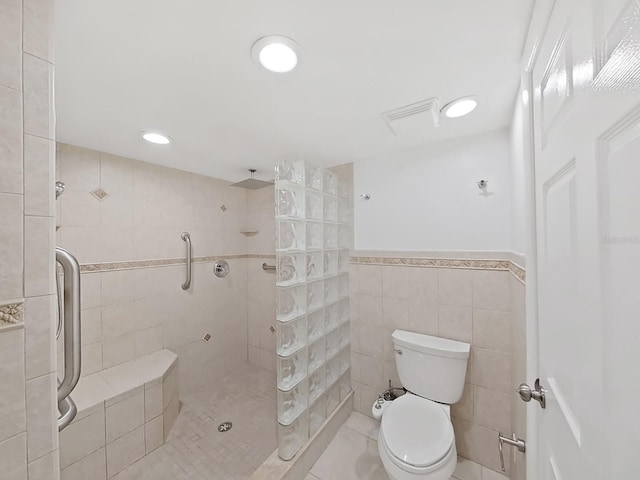 bathroom with tile patterned floors, toilet, a tile shower, and tile walls