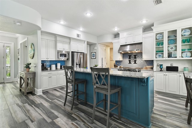 kitchen with white cabinetry, dark wood-type flooring, light stone countertops, stainless steel appliances, and a center island