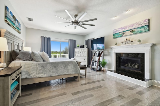 bedroom featuring a premium fireplace, wood-type flooring, ceiling fan, and a textured ceiling