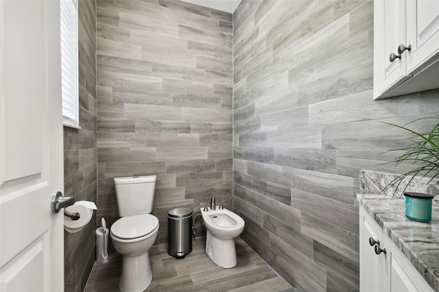 bathroom featuring tile walls, vanity, toilet, and a bidet