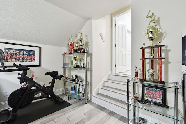 workout area with a textured ceiling, lofted ceiling, and light hardwood / wood-style flooring