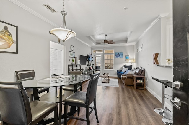 dining space featuring ceiling fan, hardwood / wood-style flooring, a raised ceiling, and crown molding