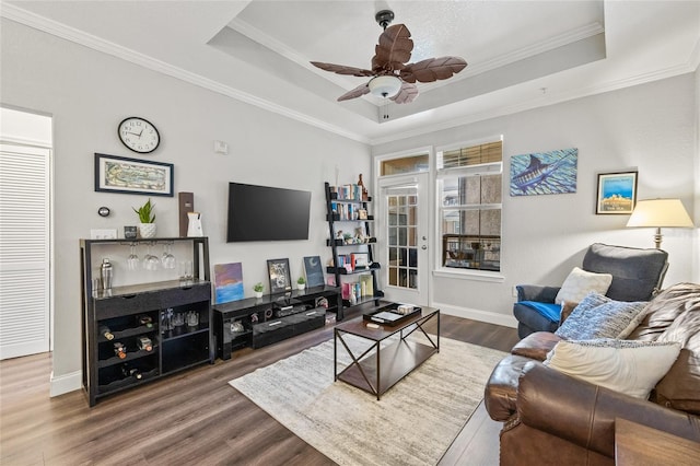 living room featuring crown molding, a tray ceiling, dark hardwood / wood-style flooring, and ceiling fan