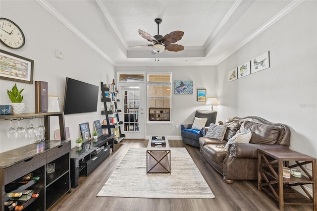 living room with ceiling fan, hardwood / wood-style flooring, a raised ceiling, and crown molding