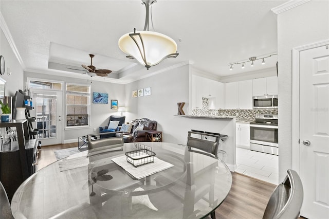 dining space with ornamental molding, light wood-type flooring, a tray ceiling, and ceiling fan