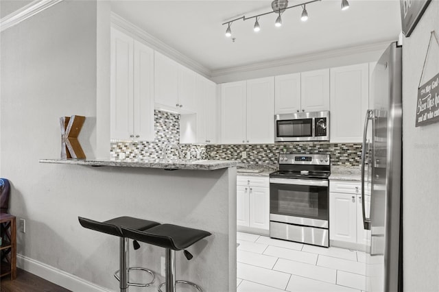 kitchen with light stone counters, tasteful backsplash, white cabinets, a kitchen breakfast bar, and stainless steel appliances