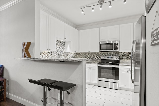 4221 W Spruce St Unit 1424, Tampa, FL 33607 - kitchen with appliances with stainless steel finishes, a breakfast bar, white cabinetry, backsplash, and light stone counters