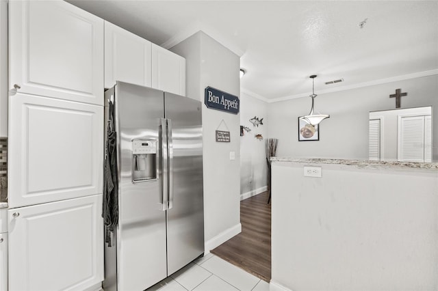 kitchen with light tile patterned flooring, stainless steel refrigerator with ice dispenser, white cabinetry, decorative light fixtures, and crown molding