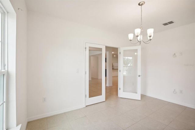 spare room featuring a chandelier, light tile patterned floors, and french doors