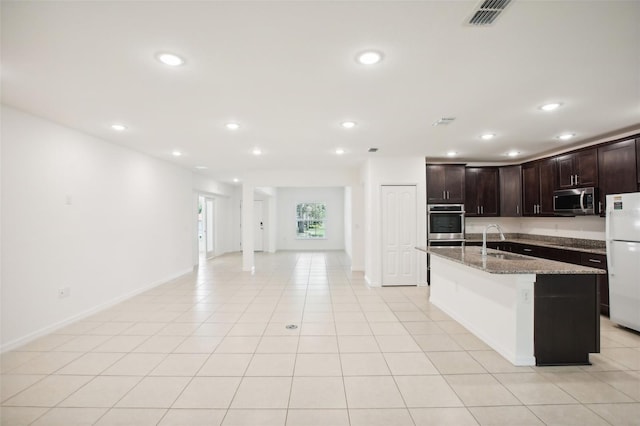 kitchen with white refrigerator, light tile patterned floors, sink, a kitchen island with sink, and dark stone counters