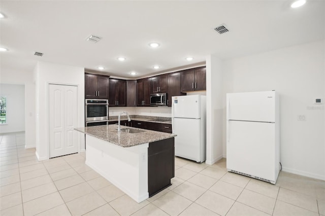 kitchen with light tile patterned flooring, sink, a center island with sink, appliances with stainless steel finishes, and dark brown cabinetry